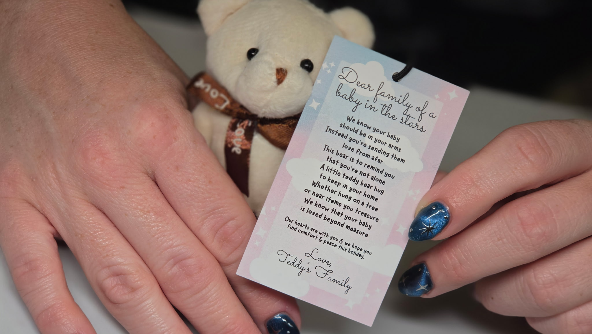 hands holding a white teddy bear ornament with ribbon and hang tag