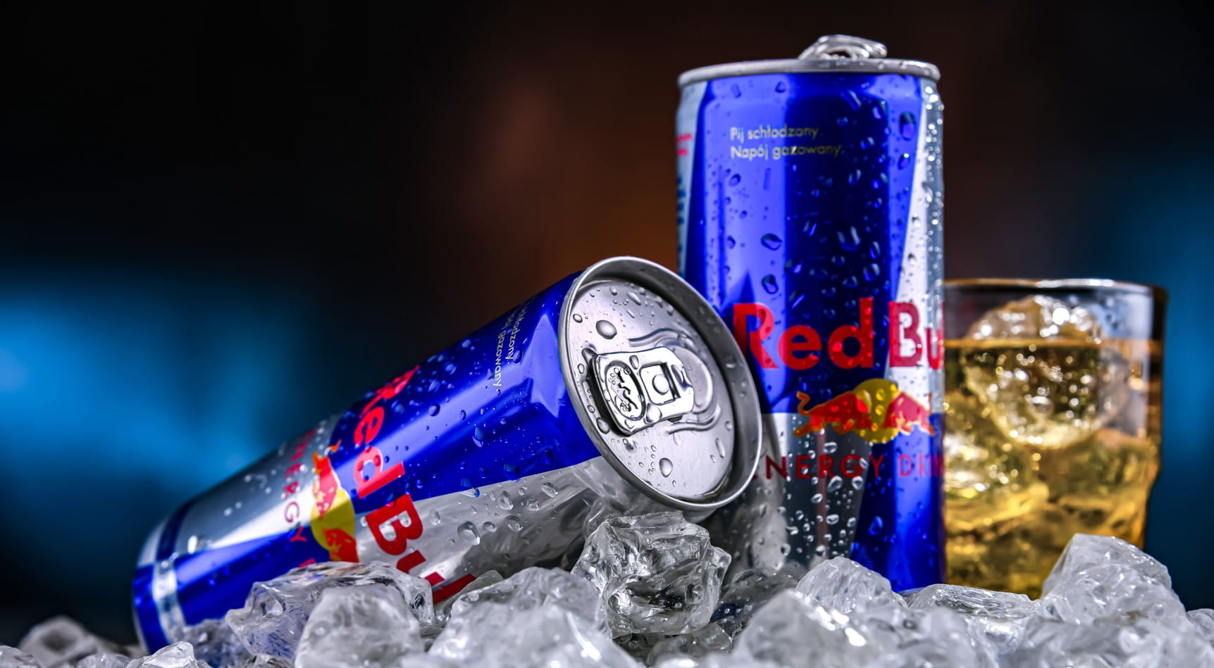 Red Bull energy drink cans resting on ice next to a filled glass