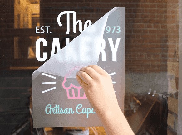 Applying a bakery window decal with cupcake branding