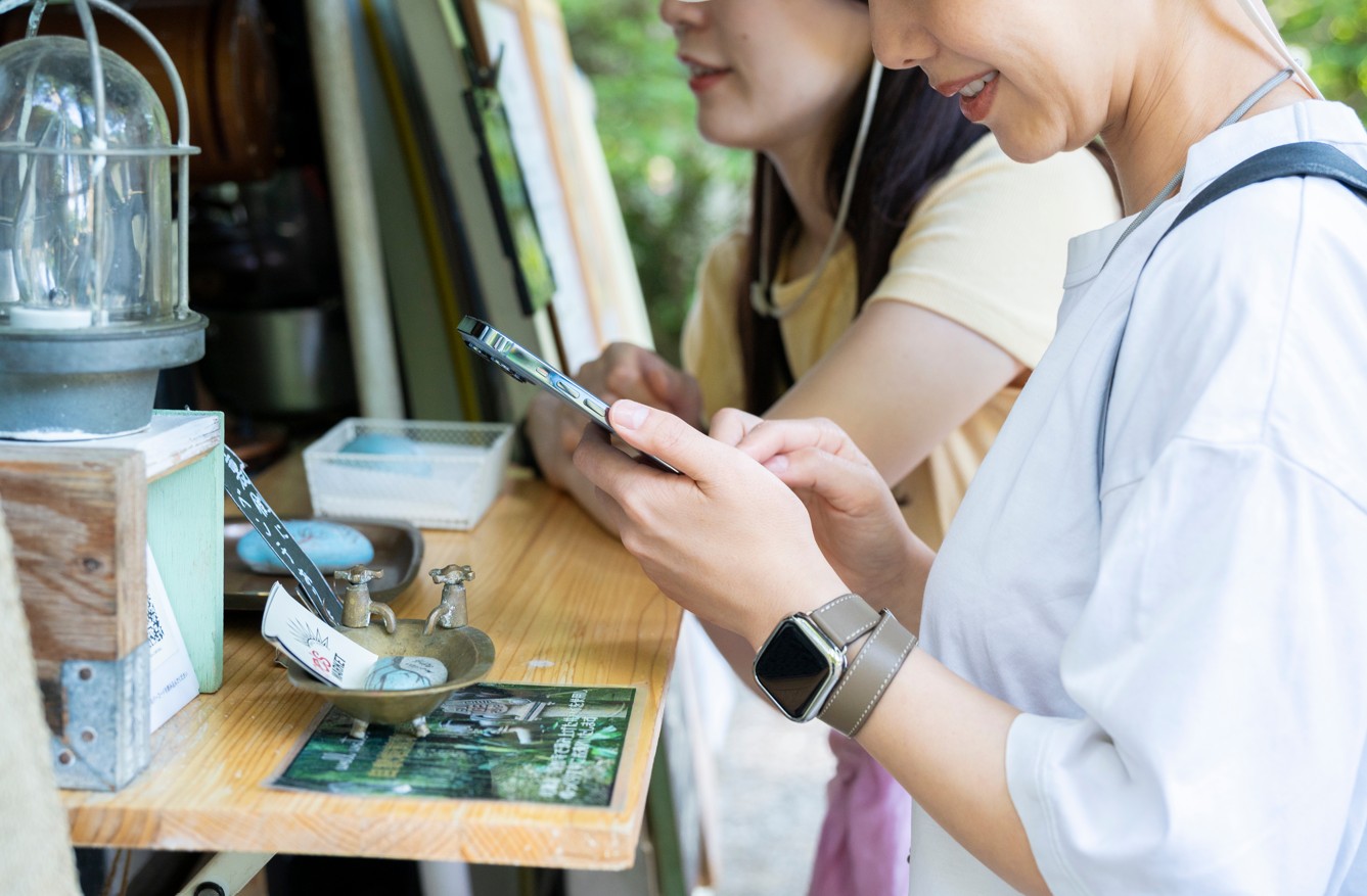 Close-up side profile of a woman using a smartphone at outdoor stall counter.
