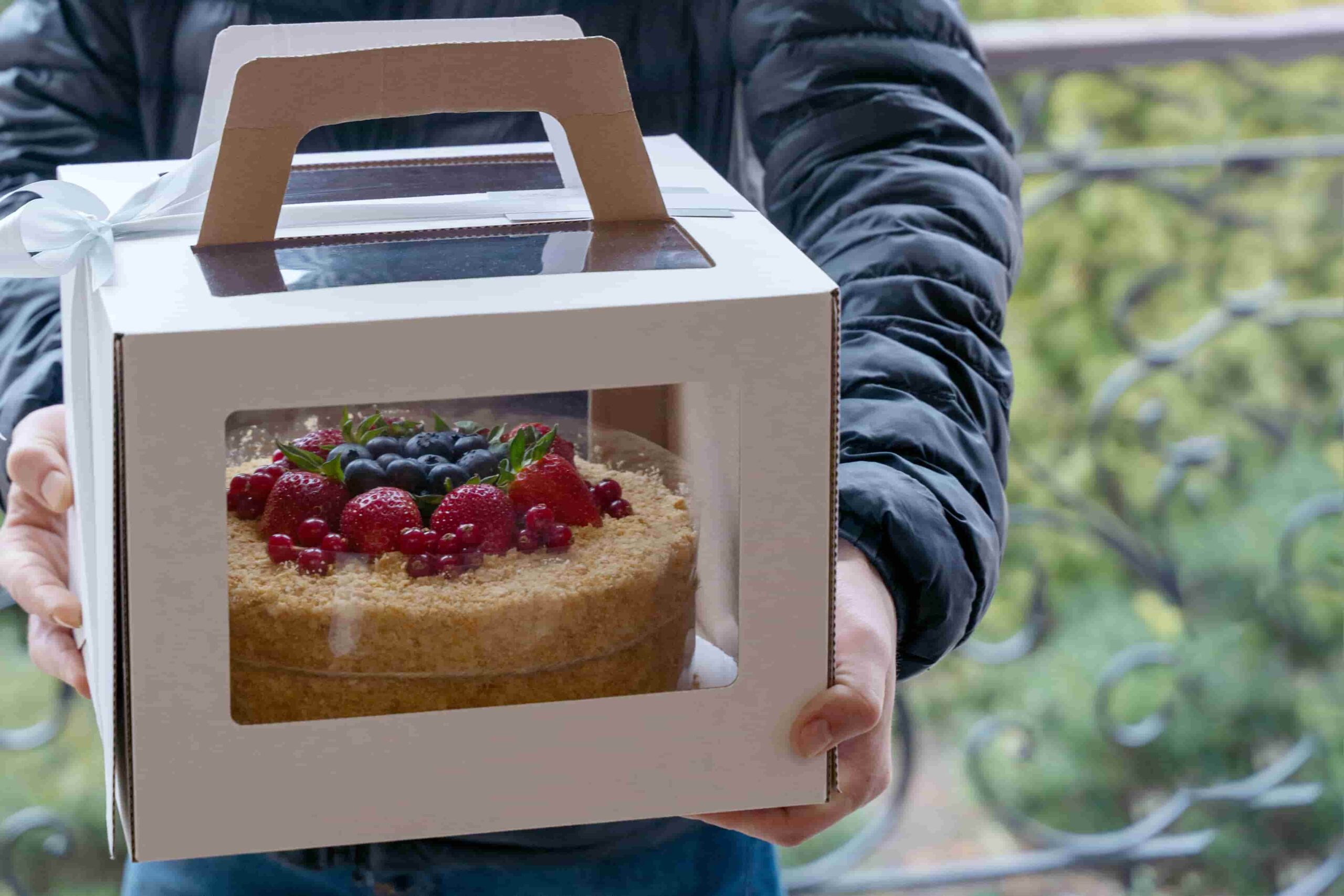 A decorated cake inside a clear handled bakery box