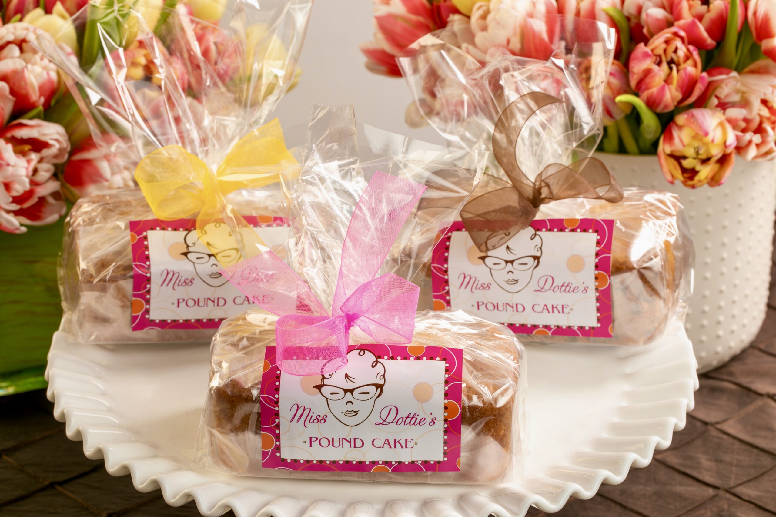 3 individually wrapped pound cakes on a plate with custom branded labels with flowers in the background